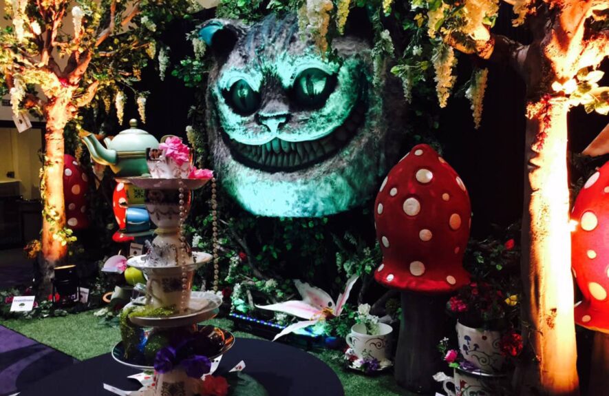 Artificial uplit wisteria trees for hire beside a Cheshire Cat face, with a tiered cake stand and giant toadstools
