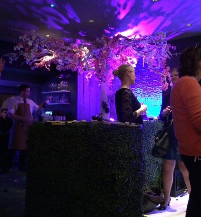 Artificial pink and white blossom arrangement for hire, overhead at an indoor drinks reception with a hedge bar