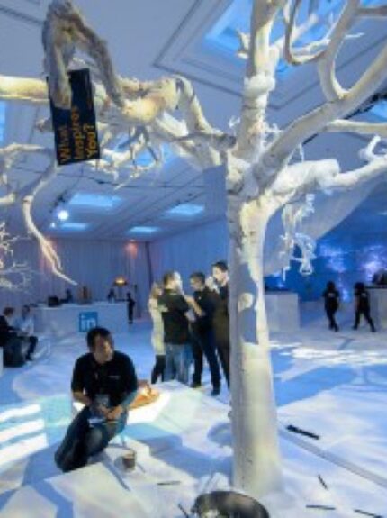Artificial white branch trees for hire, in a white snow-style room with seating blocks and a bar, guests mingling