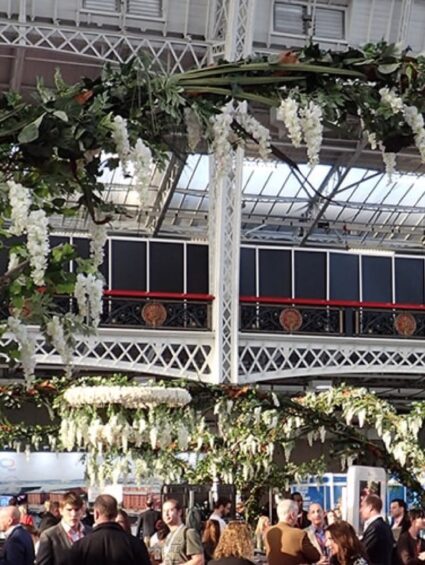 Artificial white wisteria trees for hire, arching over the crowd of a busy exhibition hall with a glass roof