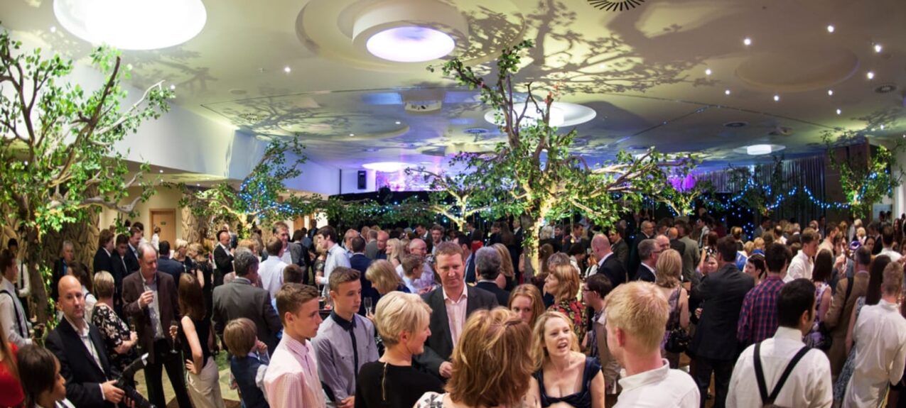 Artificial leafy trees for hire, with fairy lights, in a crowded party in a function room with leaf shadows on the ceiling