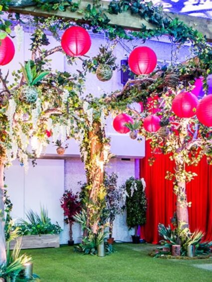Artificial trees for hire, with wisteria blooms, ivy-wrapped trunks and red paper lanterns over an artificial lawn