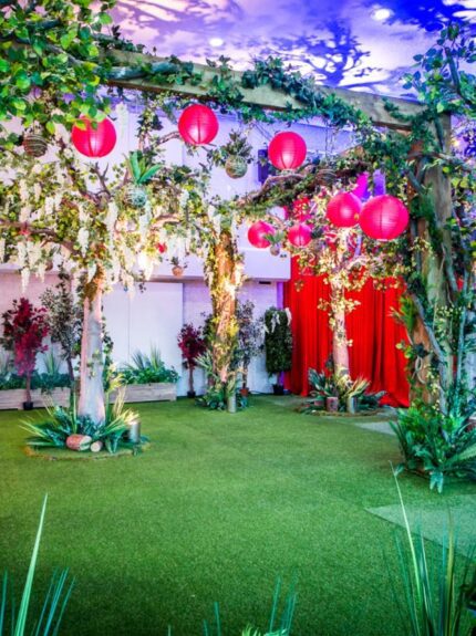Artificial wisteria trees for hire, with ivy-wrapped trunks, red lanterns and tropical plants before red curtains