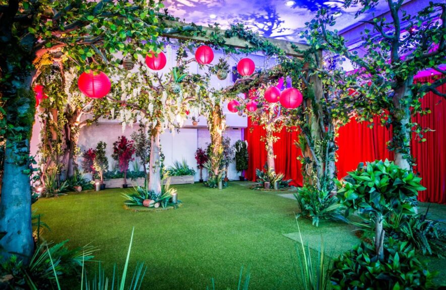 Artificial white wisteria tree for hire, ringed with tropical plants and lit from below, on an artificial lawn