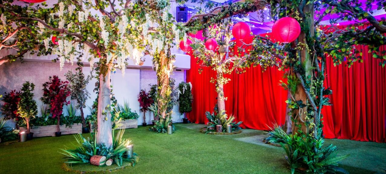 Close view of artificial wisteria trees and ivy-clad trunks for hire, with red lanterns hung overhead