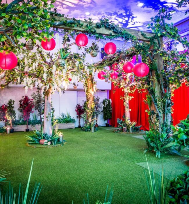 Artificial trees and potted tropical shrubs for hire, making a wooded garden under red lanterns in front of red curtains