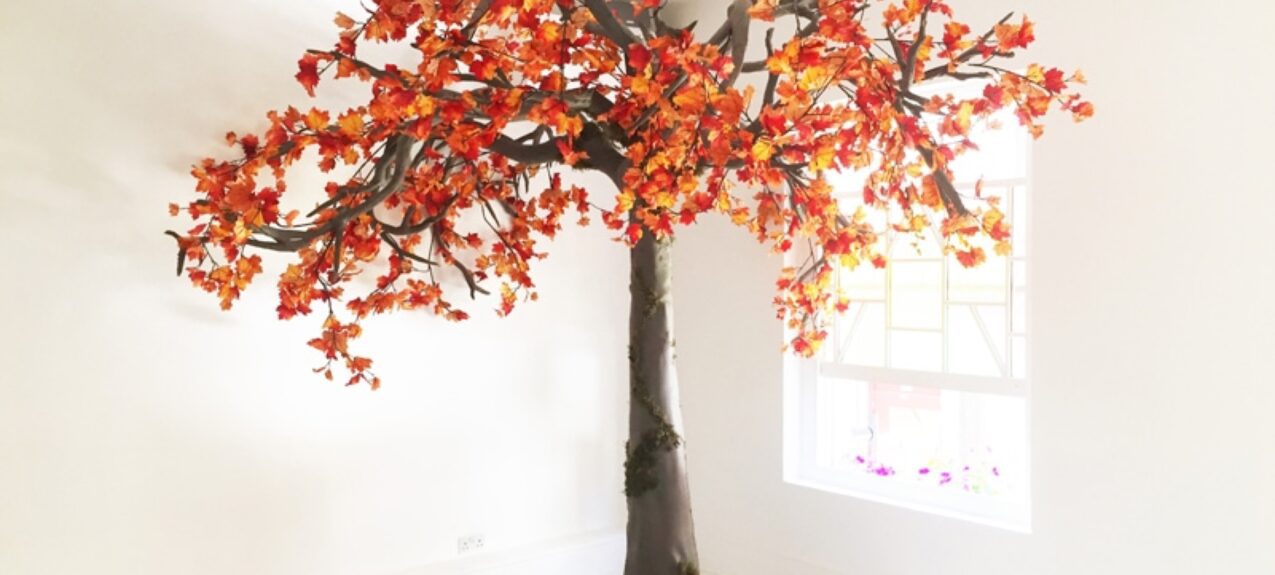 Artificial autumn tree for hire, with orange and red leaves, on a mossy base in a white room