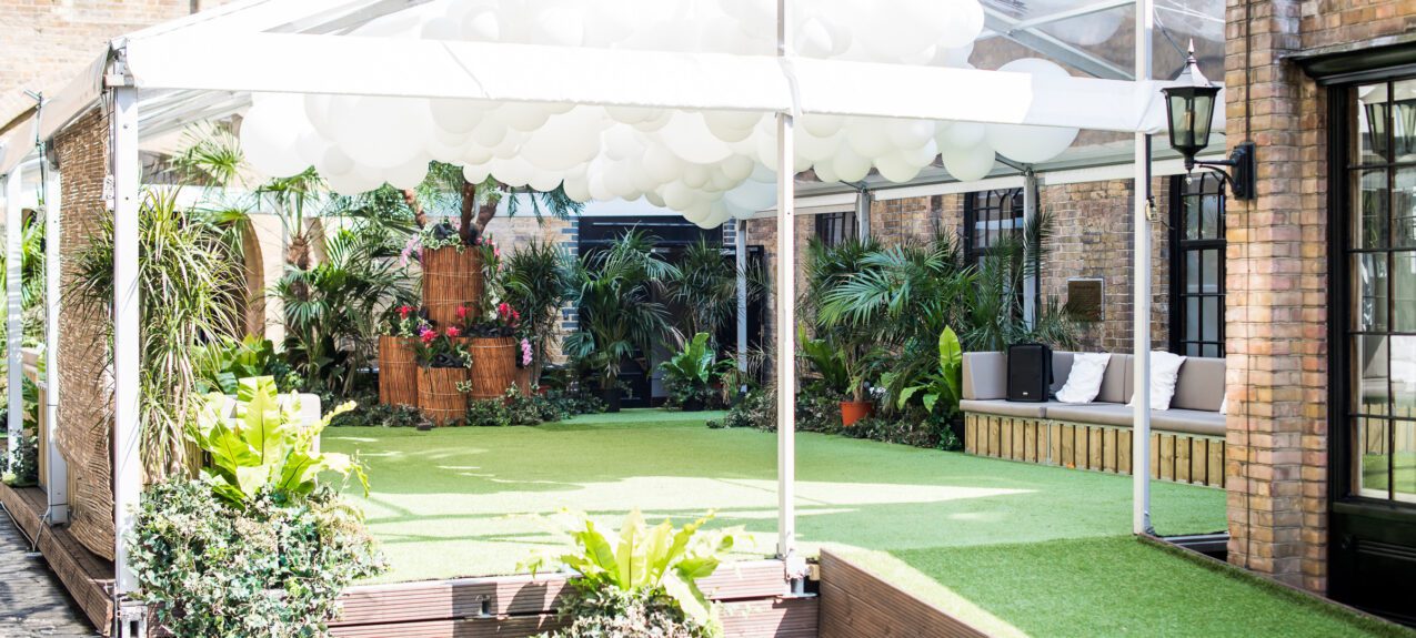 Artificial tropical plants for hire, set on an artificial lawn inside a white marquee with white balloons overhead