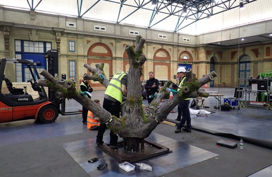 Large bespoke artificial tree for hire, mossy trunk and bare branch stumps being built by crew before leaves go on