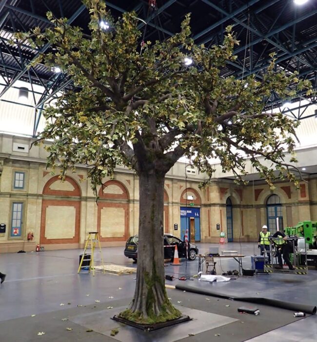 Large artificial tree for hire, mossy trunk and wide leafy canopy, in the middle of an empty exhibition hall