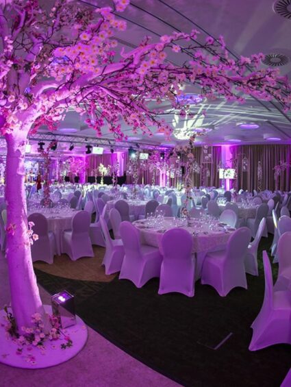 Artificial cherry blossom tree for hire, uplit purple in a ballroom of round tables with white chair covers