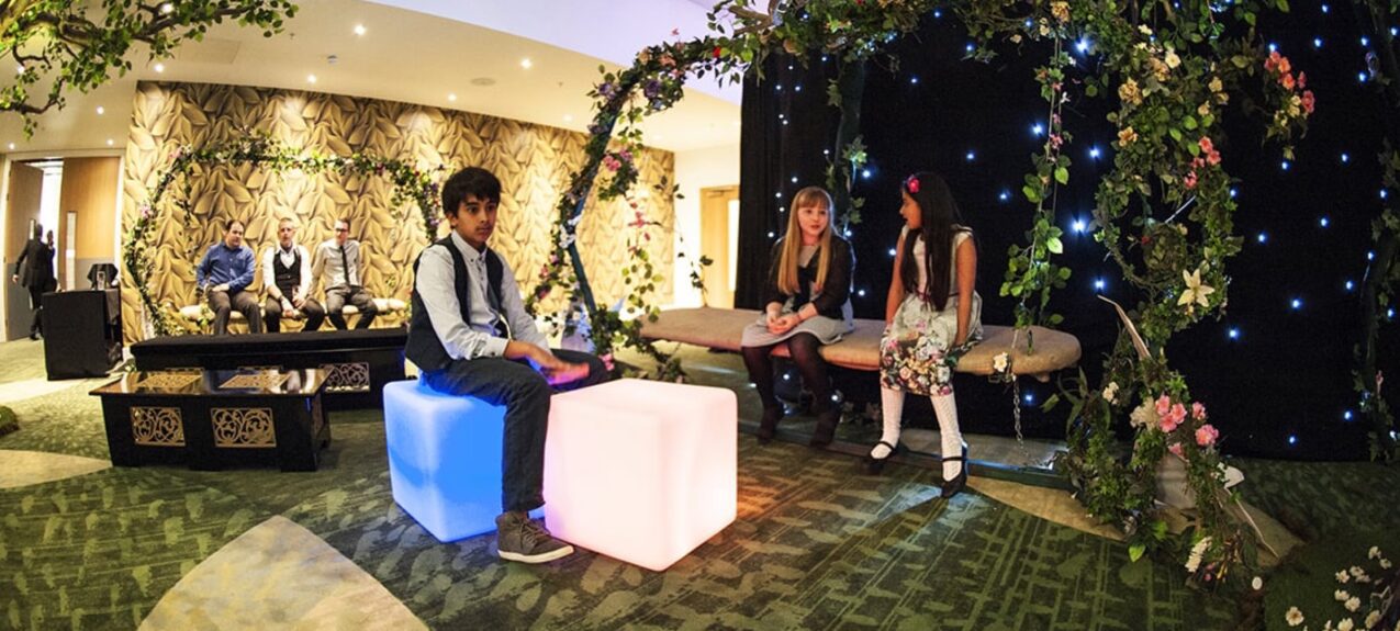 Artificial flower and ivy arches for hire, over cube seats and a starlit backdrop in a green carpeted lounge