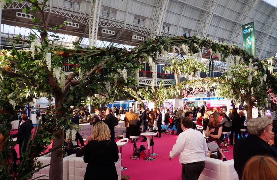 Artificial white wisteria trees for hire, arching over a pink carpeted exhibition aisle and visitors under a glass roof