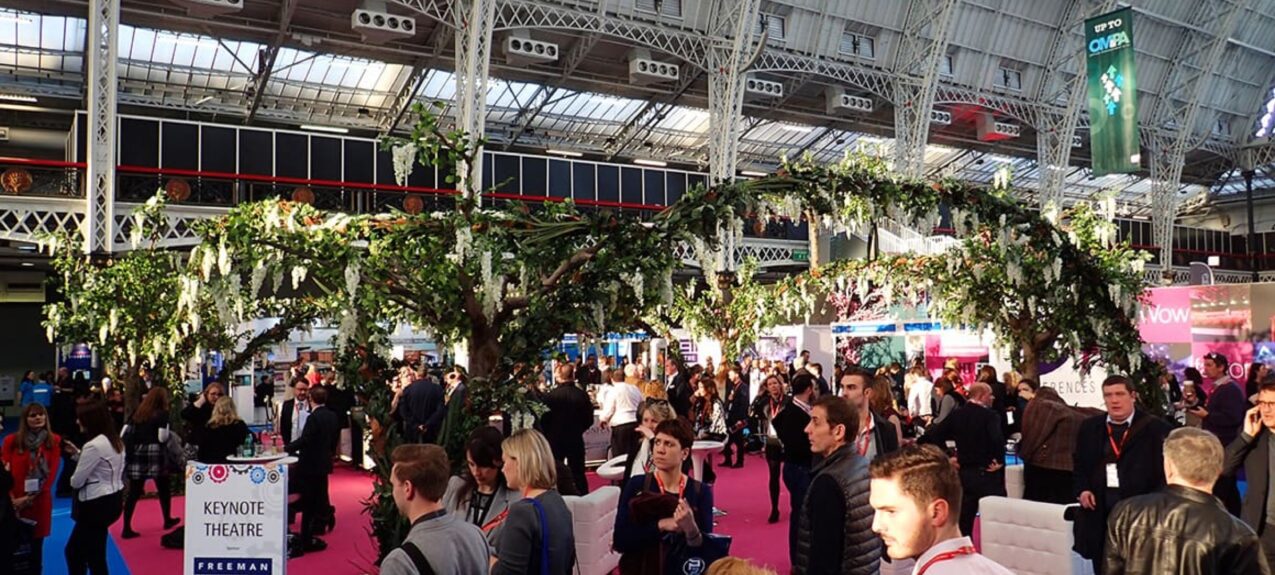 Artificial white wisteria trees for hire, arching over an exhibition crowd near a Keynote Theatre sign