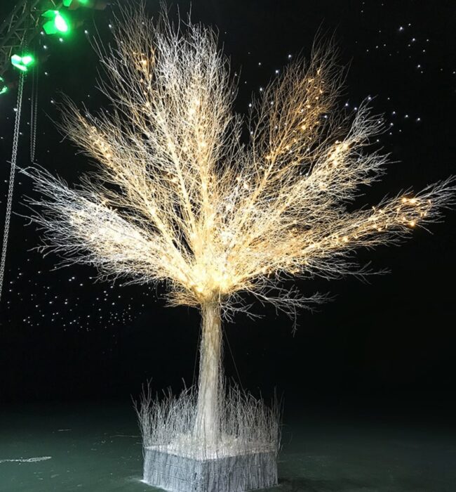 Artificial white branch tree for hire, wrapped in warm fairy lights in a planter under green spotlights