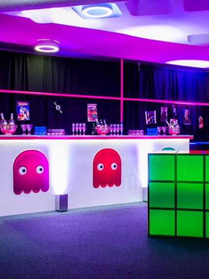 Retro arcade-themed white bar with pink ghost graphics, a glowing green cube and vinyl records, under pink lighting