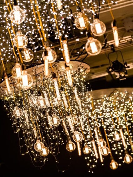 Hanging fairy light and filament bulb chandeliers overhead in a dark event room