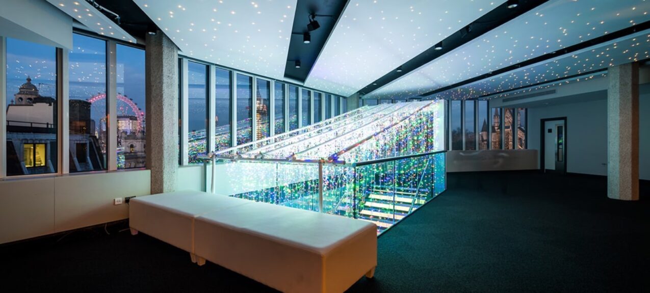 Starry ceiling lights and a fairy light curtain over a staircase in a room with a white bench and London Eye view