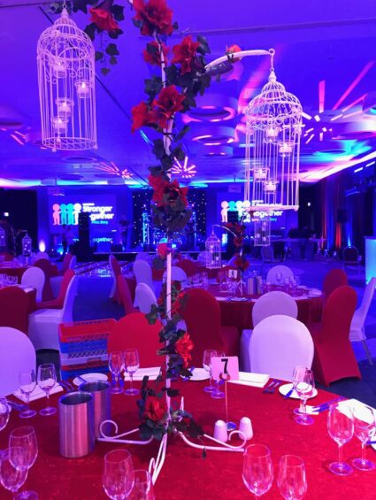 Artificial red roses wound up poles, with white birdcages, for hire over banquet tables, Stronger Together stage behind