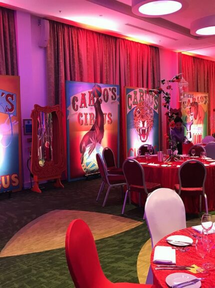 Painted "Carlo's Circus" boards in a red-lit banquet room with red curtains and red-covered tables