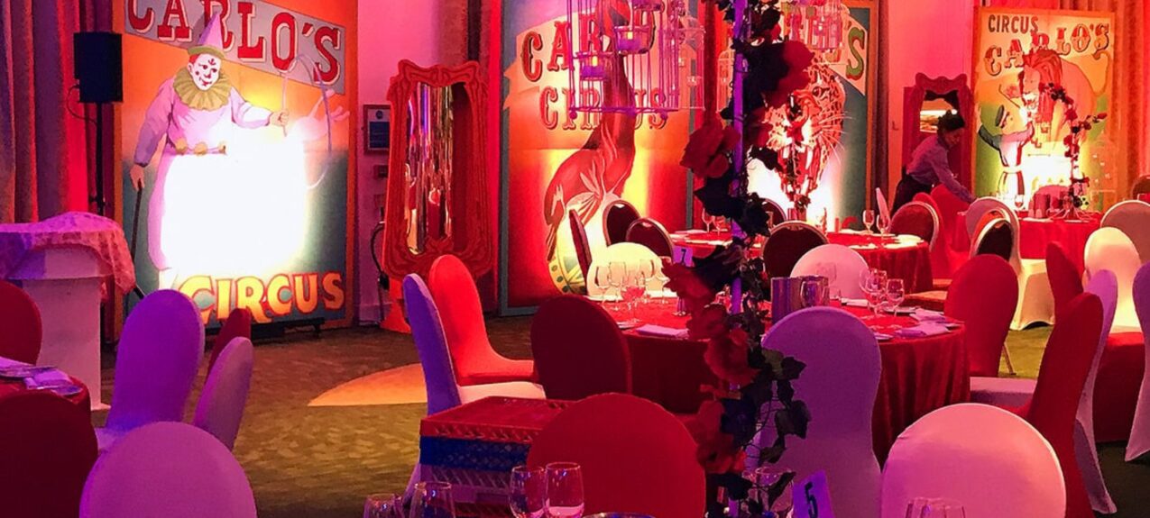 Artificial rose-wound pole and white birdcage for hire in front of Carlo's Circus boards and red-covered tables