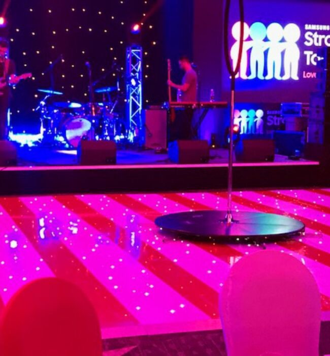 Live band on a stage beside a pink starlit dance floor and a Samsung Stronger Together screen
