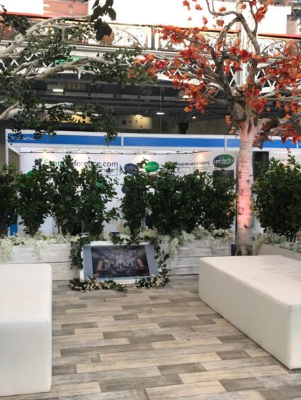 Artificial trees and hedge planters for hire, on an exhibition stand with white seating blocks and wood-effect flooring