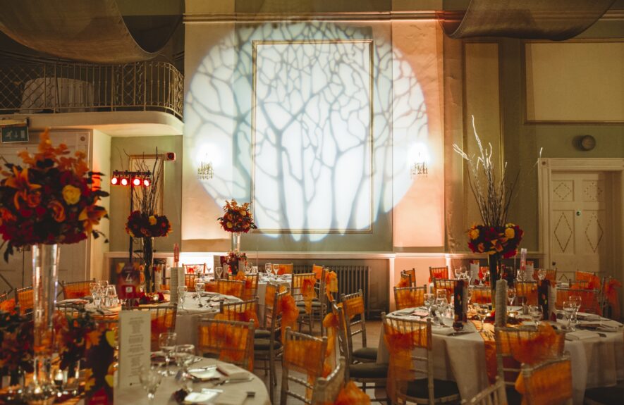 Artificial tall autumn flower centrepieces for hire, on dinner tables in a ballroom with a tree branch projection on the wall