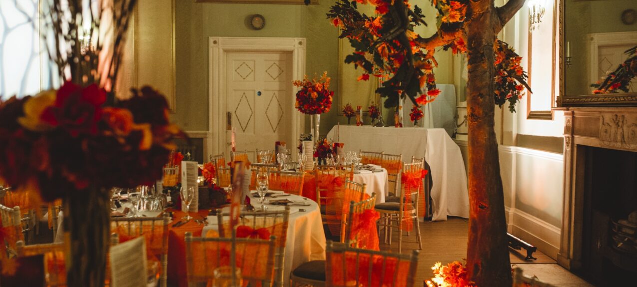 Artificial autumn tree with orange and red leaves for hire, uplit in a ballroom beside dining tables