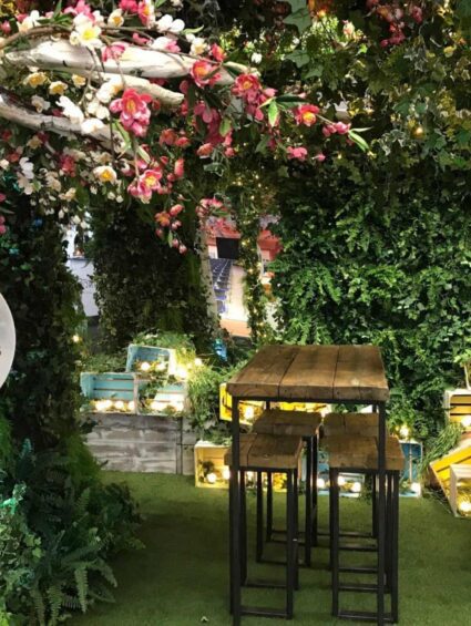 Artificial flower and ivy arch for hire, installed on an exhibition stand with fairy lights, crates and a high table