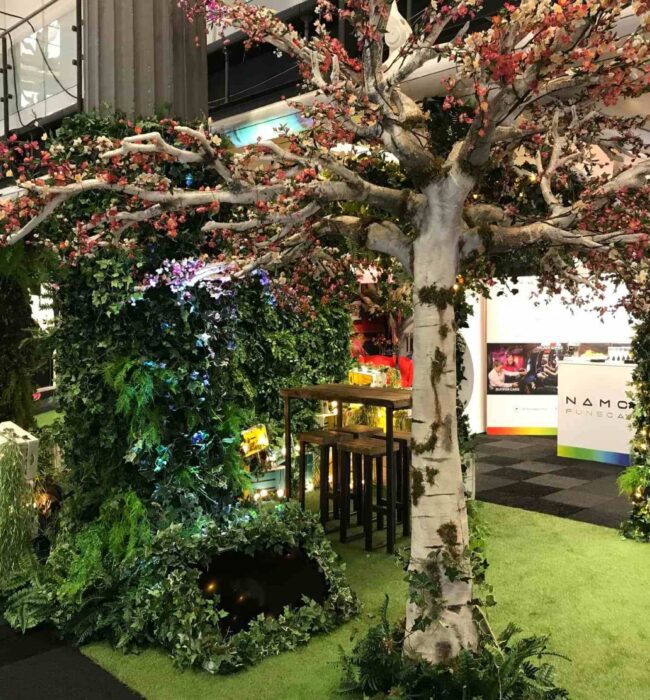 Artificial birch blossom tree and ivy wall for hire, placed on artificial grass beside a high table at an exhibition