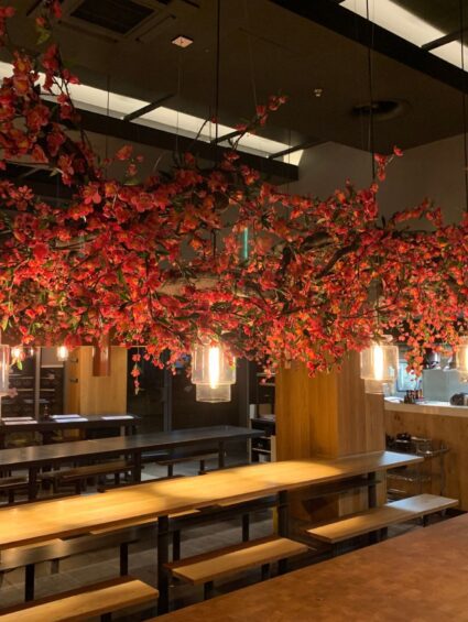 Red artificial blossom branches for hire, installed overhead above restaurant dining tables with glass pendant lights
