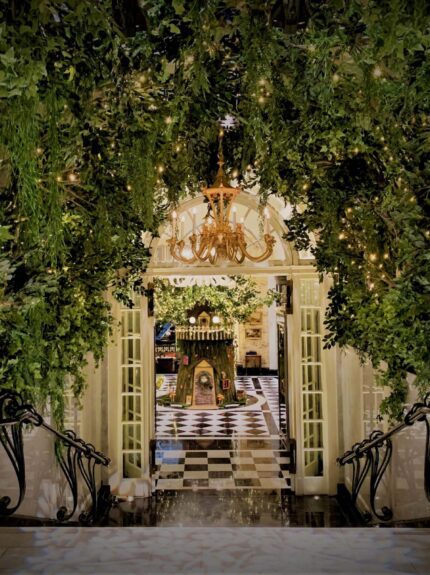 Artificial leafy foliage arch with fairy lights for hire, framing a Savoy Hotel doorway and chandelier