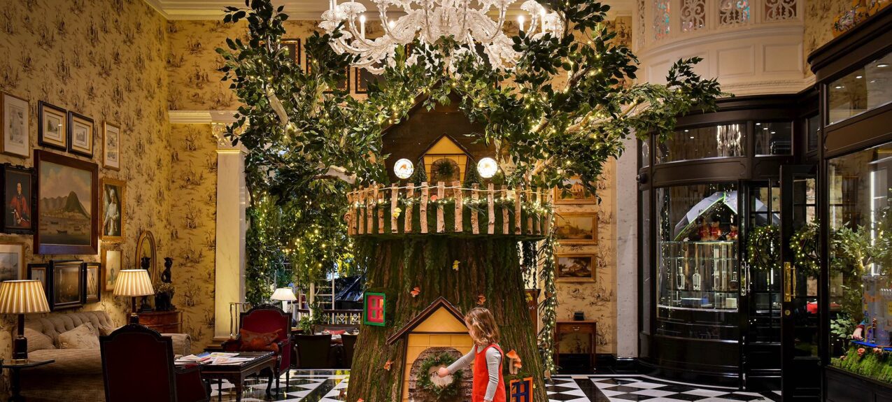 Giant tree stump house with a child at its door, beneath an artificial tree and chandelier at the Savoy Hotel