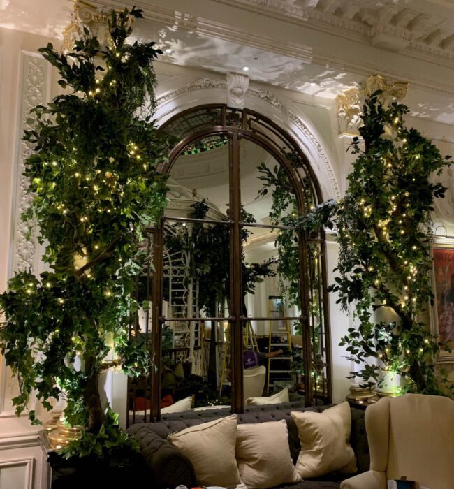 Two artificial trees with fairy lights for hire, flanking an arched mirror and sofa at the Savoy Hotel