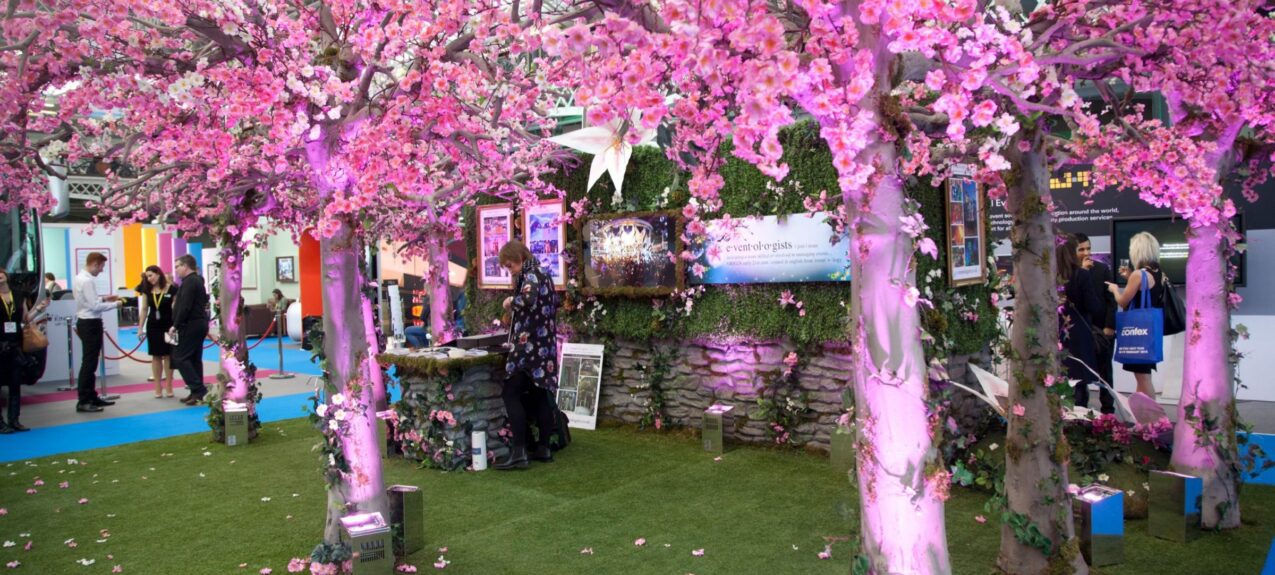 Pink artificial cherry blossom trees for hire, uplit on artificial grass on an exhibition stand with fallen petals