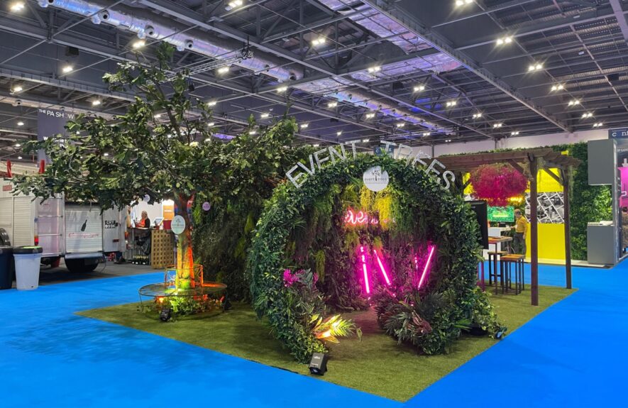 Artificial foliage ring for hire spelling EVENT TREES, with pink neon lights and a tree, on a Confex stand