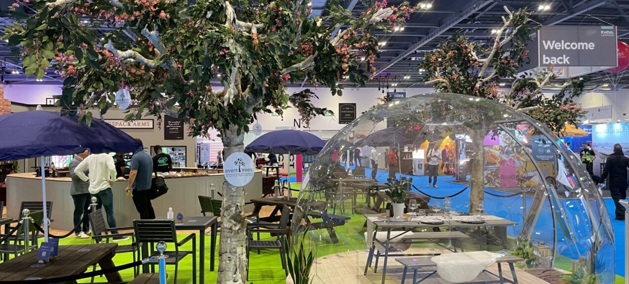 Artificial blossom tree for hire beside a clear dome and picnic benches on green grass, with a Welcome back sign