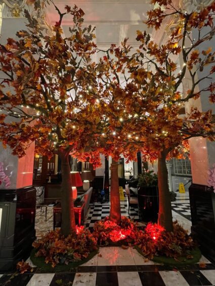 Artificial autumn trees with orange and rust leaves for hire, with fairy lights in the Savoy Hotel foyer, checkered floor