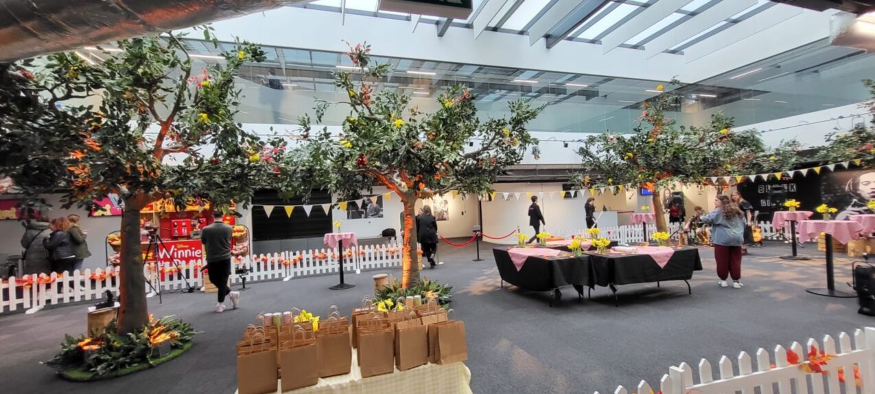 Artificial trees for hire, placed in an indoor atrium with white picket fencing, bunting and pink-clothed tables
