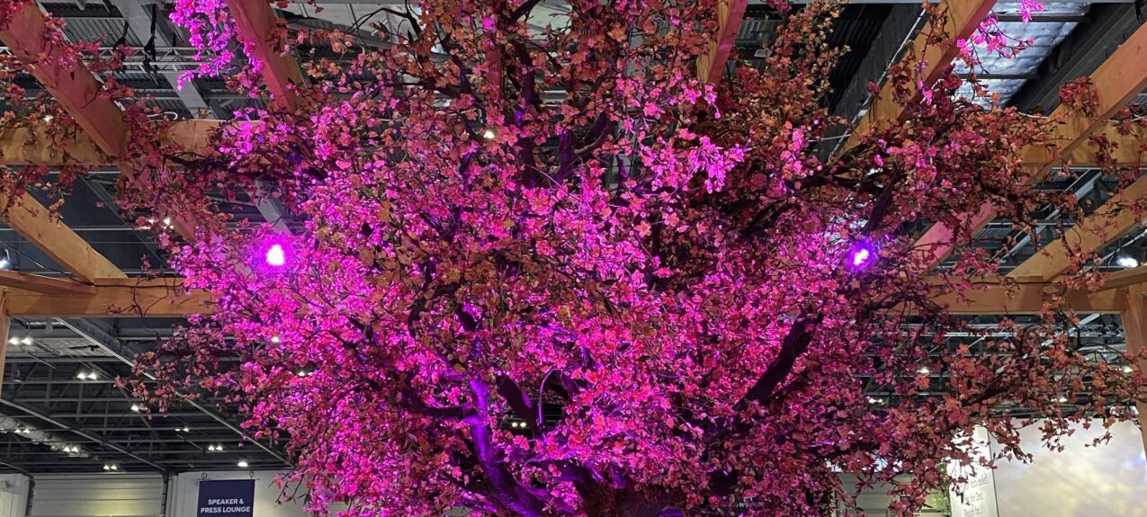Artificial cherry blossom tree for hire, pink-lit in a timber counter ring under the 'Zenrelia' sign, London Vet Show
