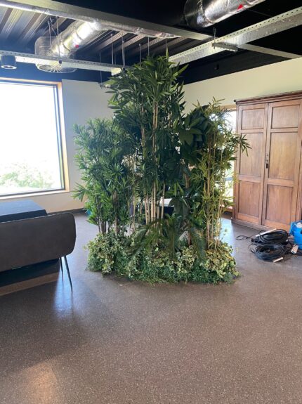 Artificial bamboo and foliage screen for hire, in a clump on a leafy base in a modern event space with exposed ceiling