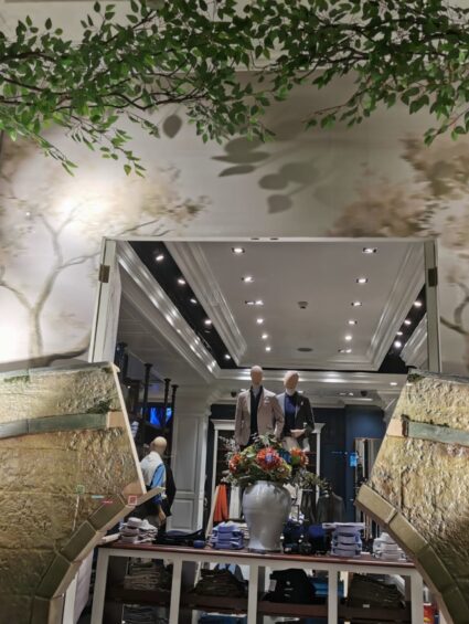 Artificial leafy tree branches for hire, hung across a Sloane Street shop window above stone-effect walls and mannequins