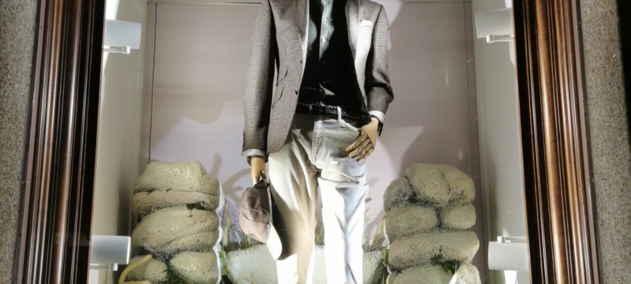 Artificial leafy tree branch for hire, above a mannequin among mossy stones in an arched shop window