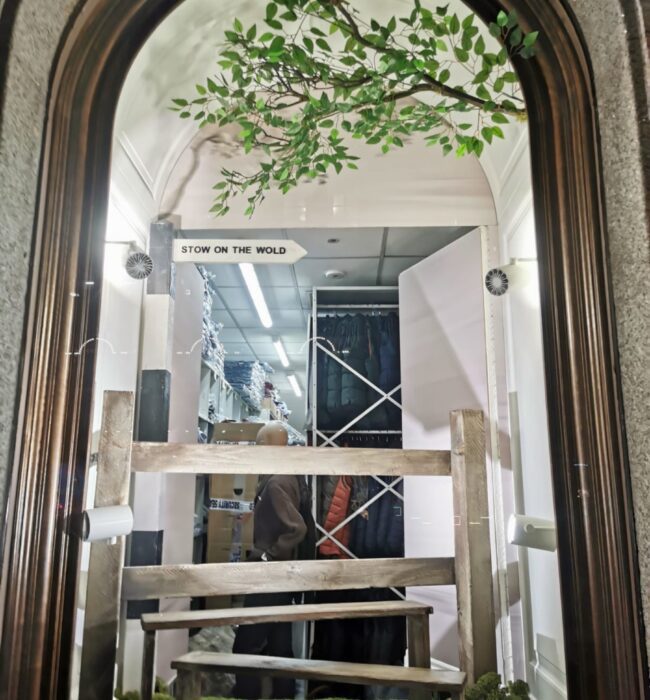 Artificial leafy branch for hire, over a wooden stile and moss in an arched window with a 'Stow on the Wold' sign