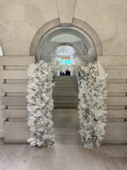 Artificial frosted white foliage arch for hire, at a stone building entrance with steps behind, One Moorgate
