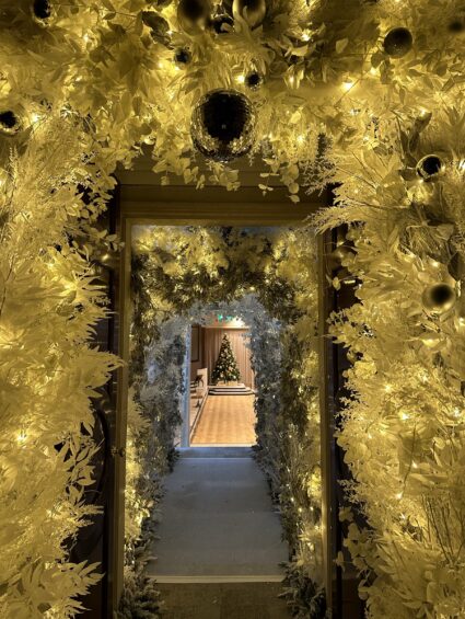 Artificial gold and white foliage tunnel for hire, with baubles and fairy lights, leading to a Christmas tree at One Moorgate