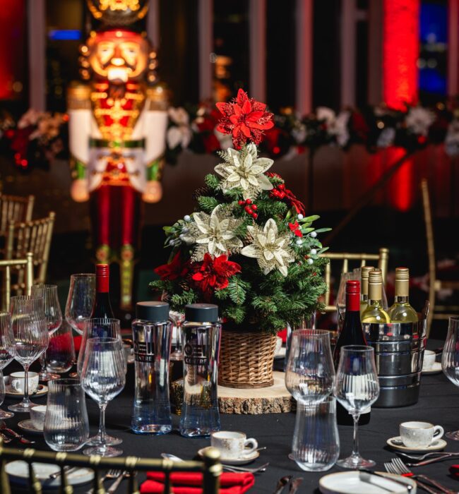 Artificial mini Christmas tree table centre with poinsettias, for hire, beside a nutcracker statue and black table linen