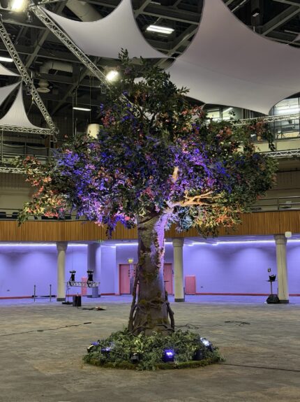 Large artificial blossom tree for hire, on a mossy base ringed with purple uplighters in a conference hall