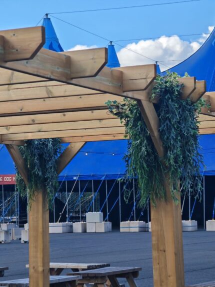 Artificial trailing foliage for hire, hung from pergola posts and beams in front of a blue big-top tent, Download Festival